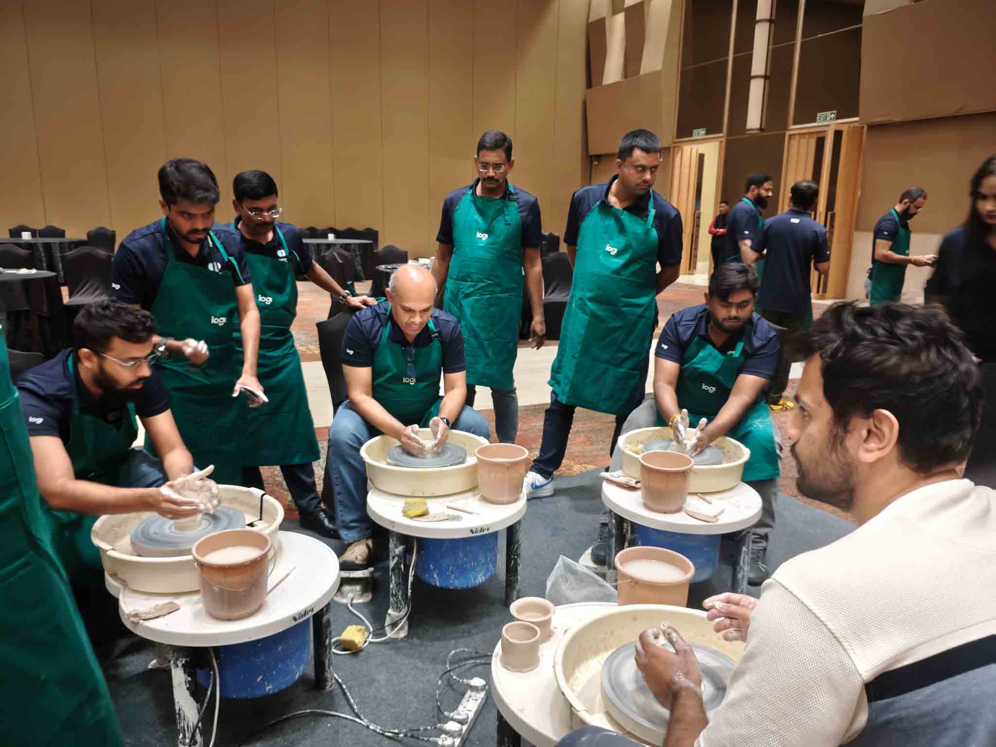Participants wearing aprons engaged in pottery wheel activities during a workshop session.